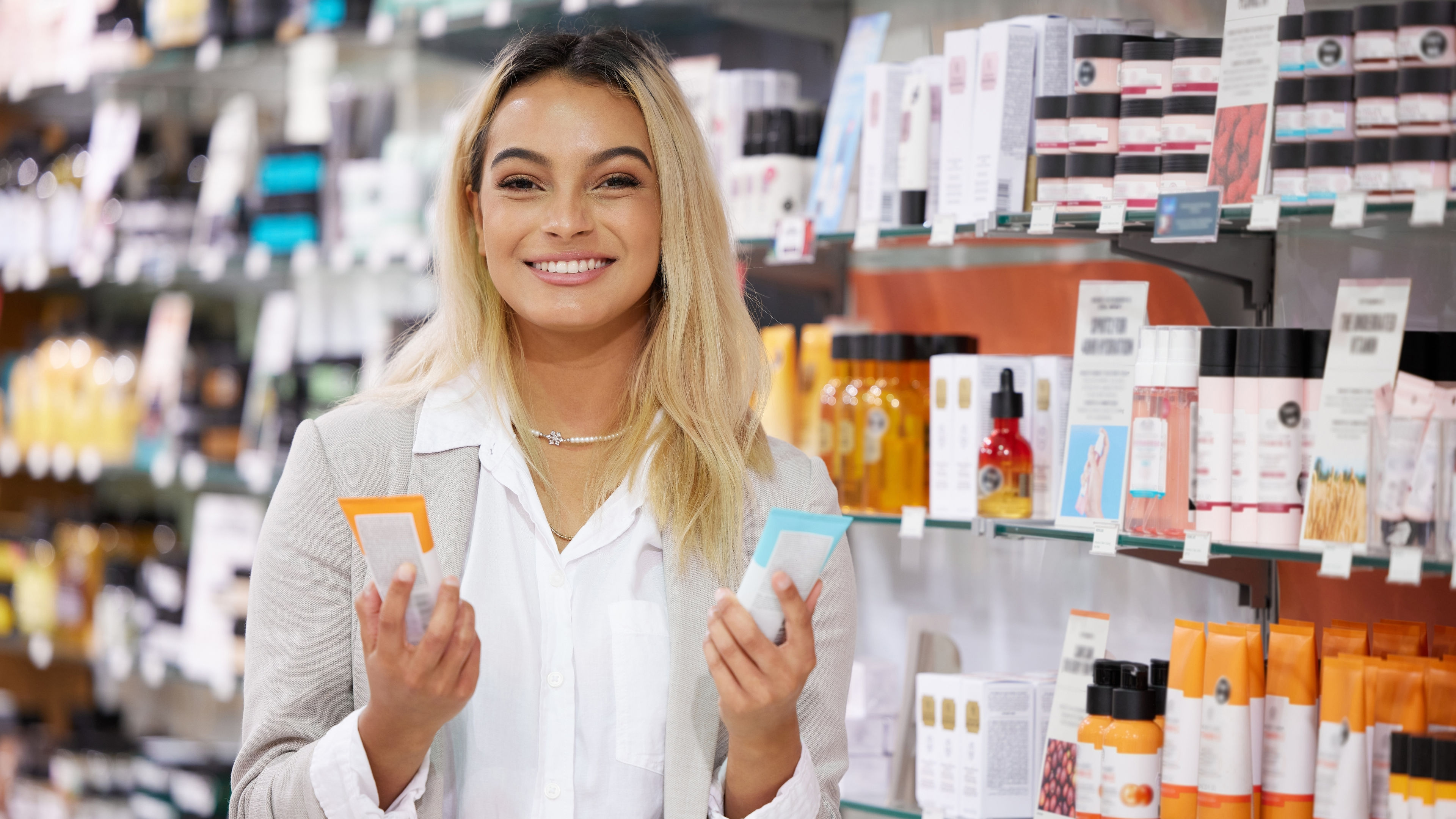 A portrait of a young woman standing inside a store, holding beauty products in her hands.