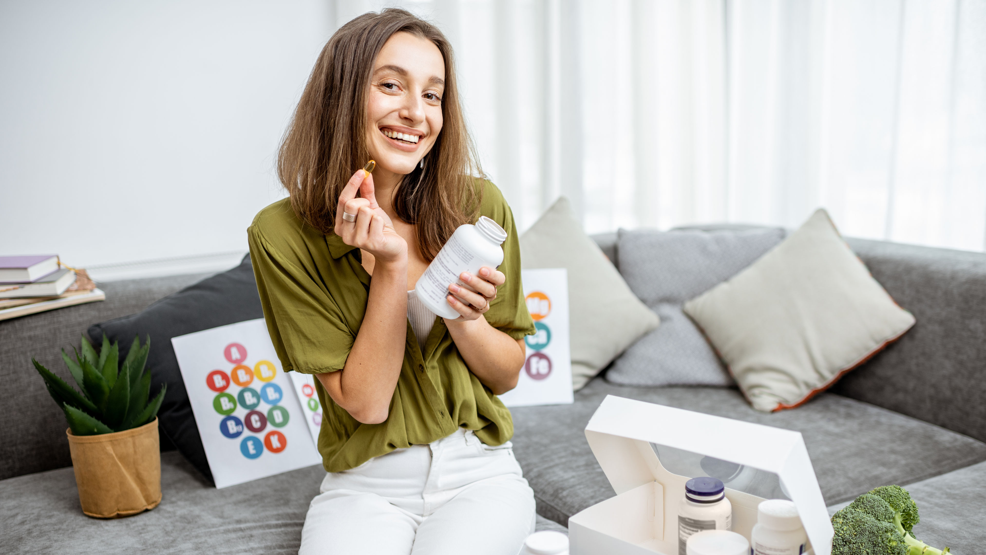 A cheerful woman is holding a supplement capsule