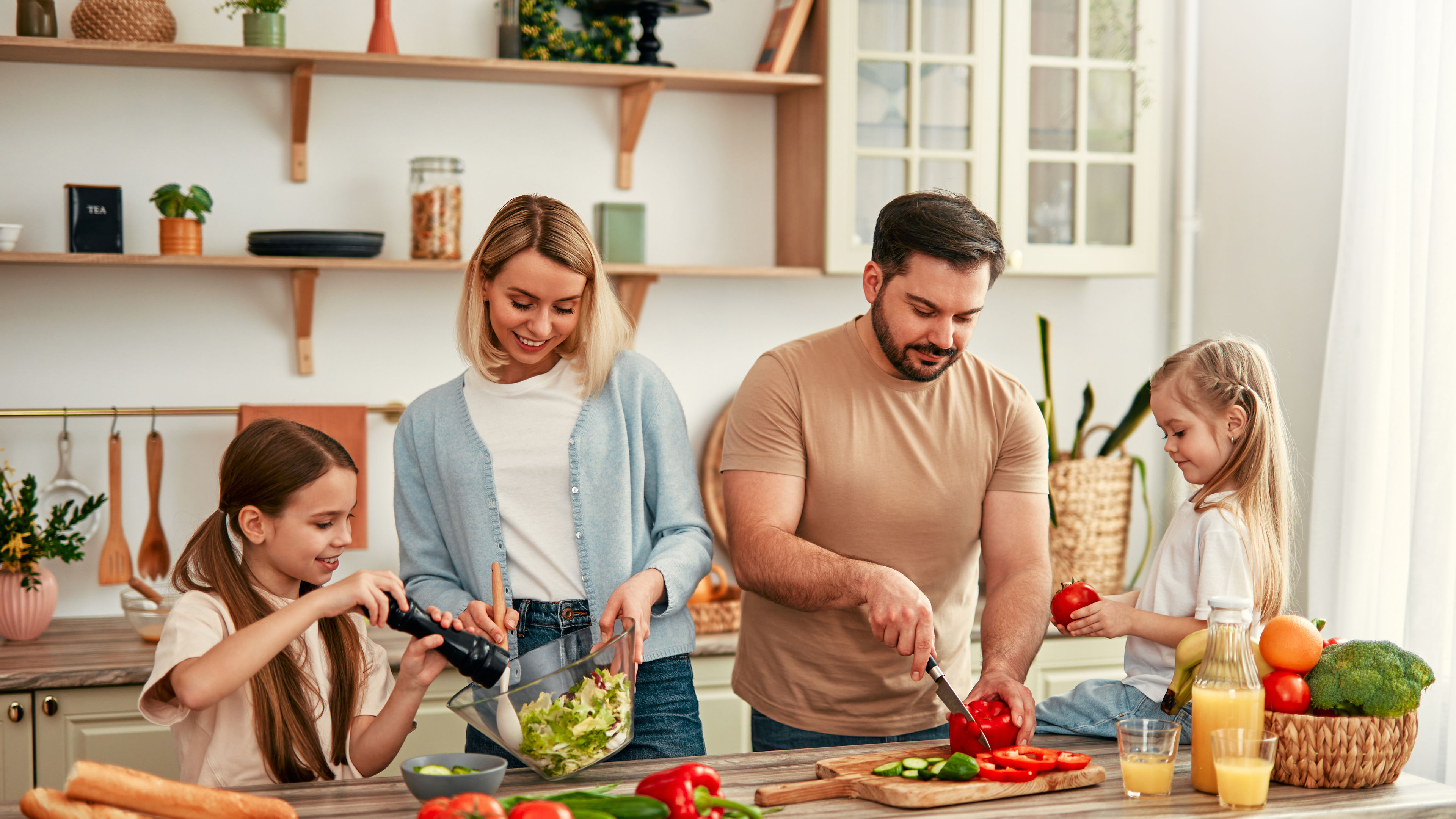 A happy family of four is cooking together in a bright kitchen