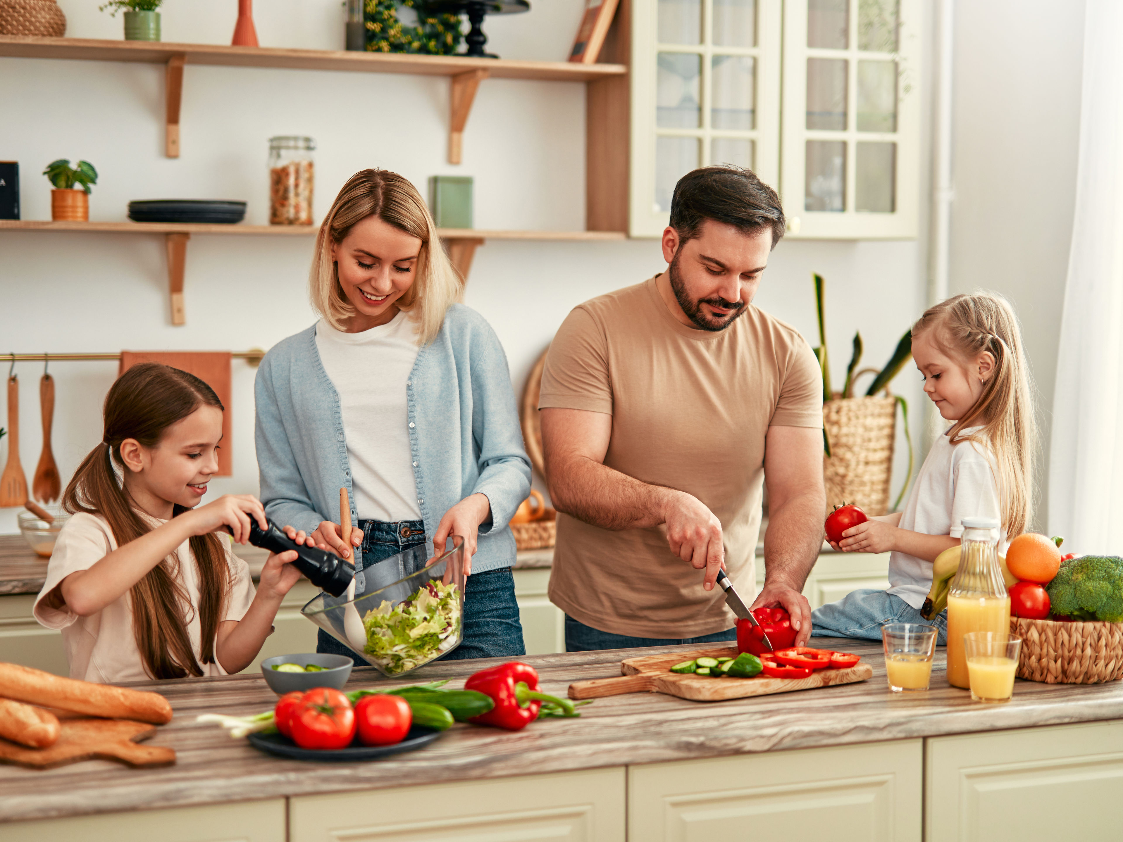 A happy family of four is cooking together in a bright kitchen