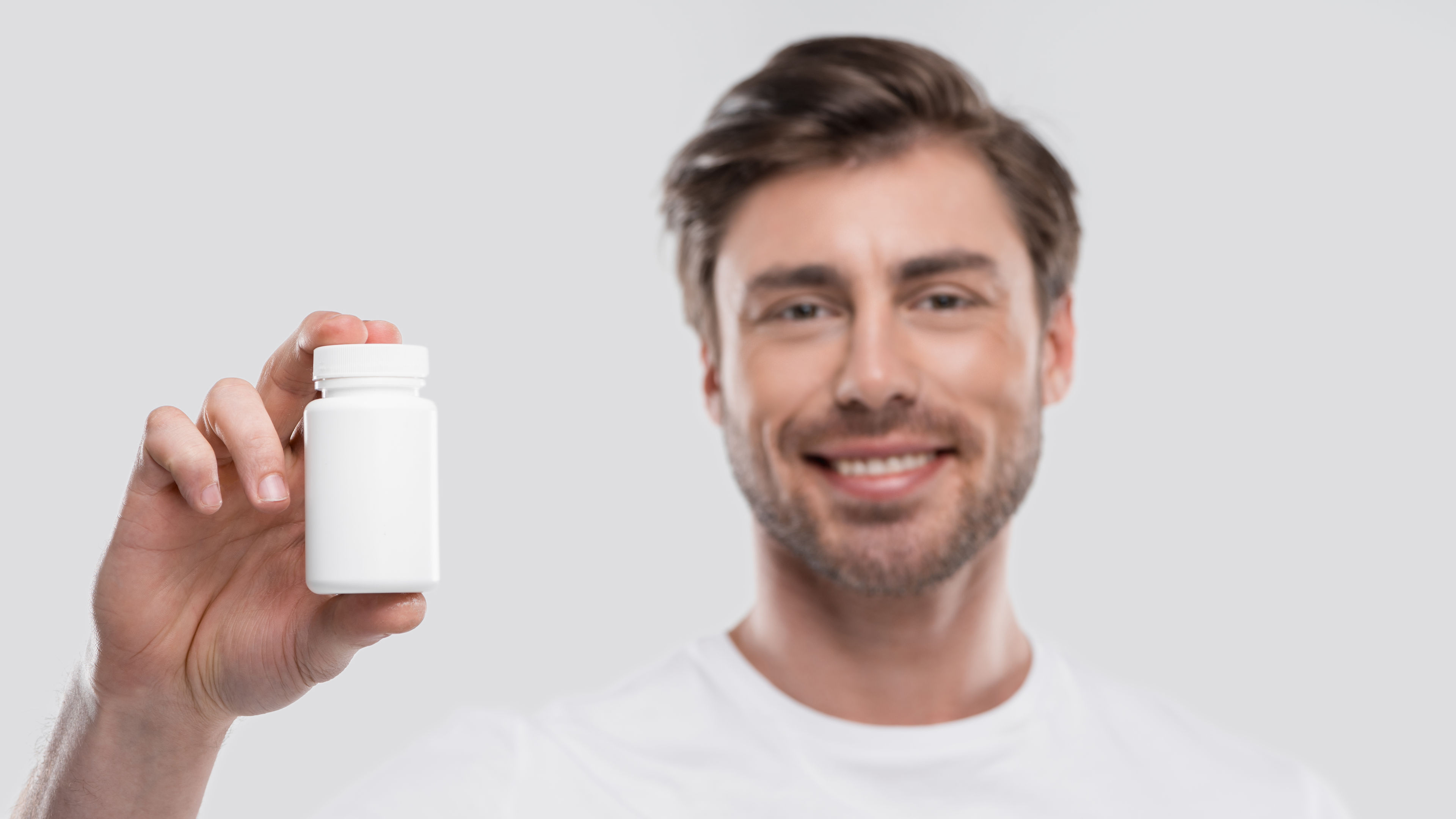 A smiling man holding up a white bottle of supplements.
