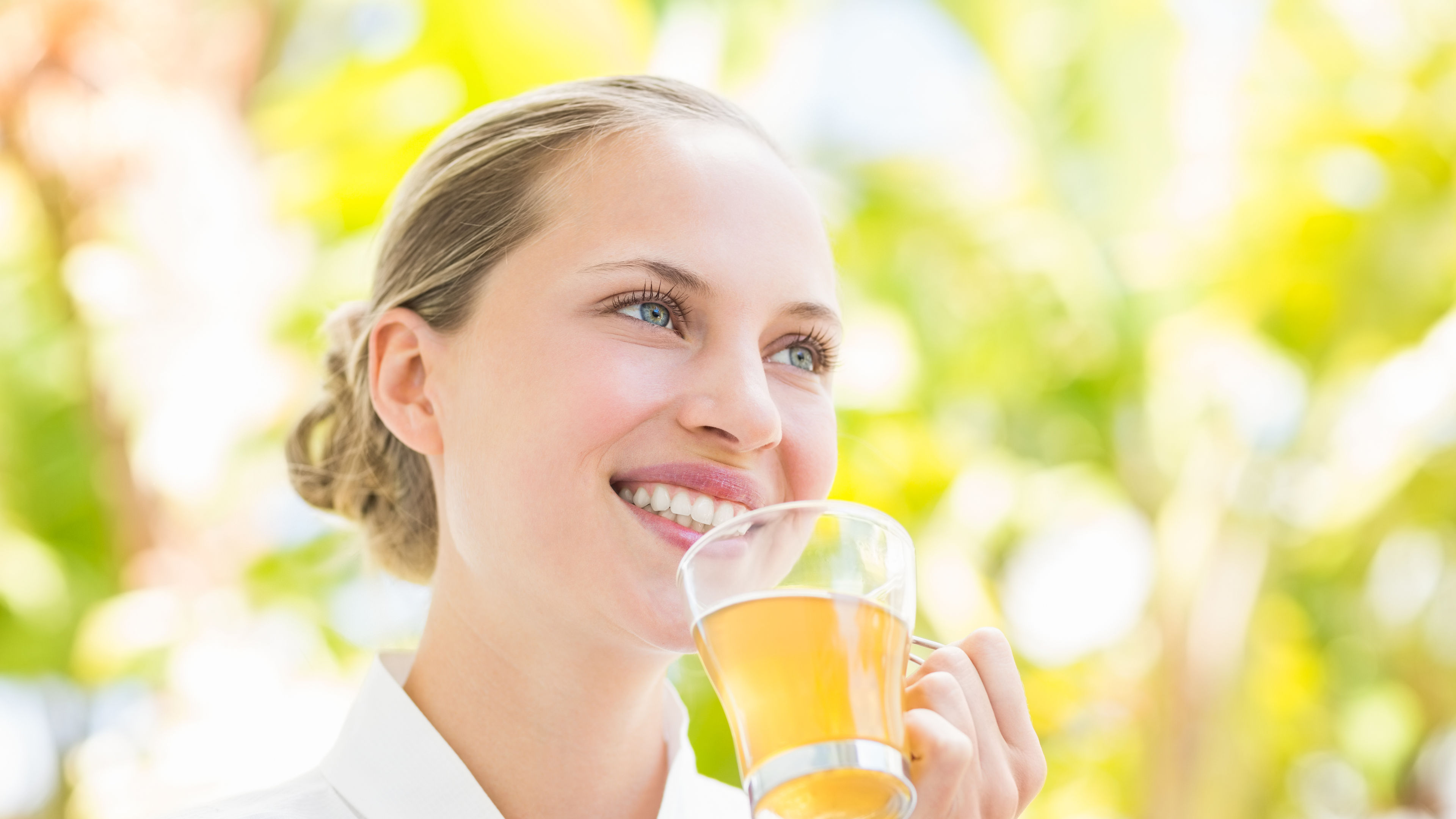 A smiling woman is holding a glass cup of tea