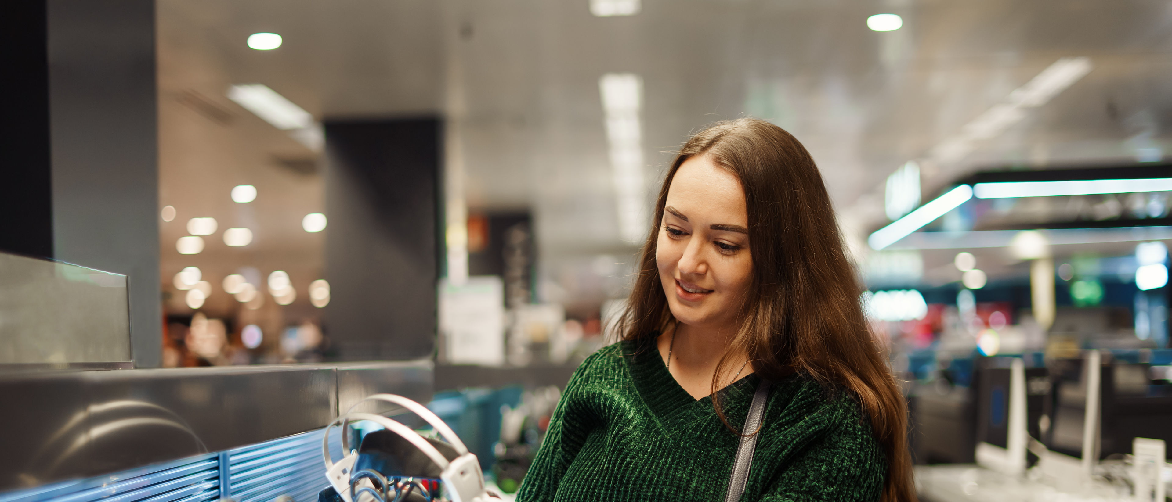 Cheerful young woman buying new headphones in tech store department.