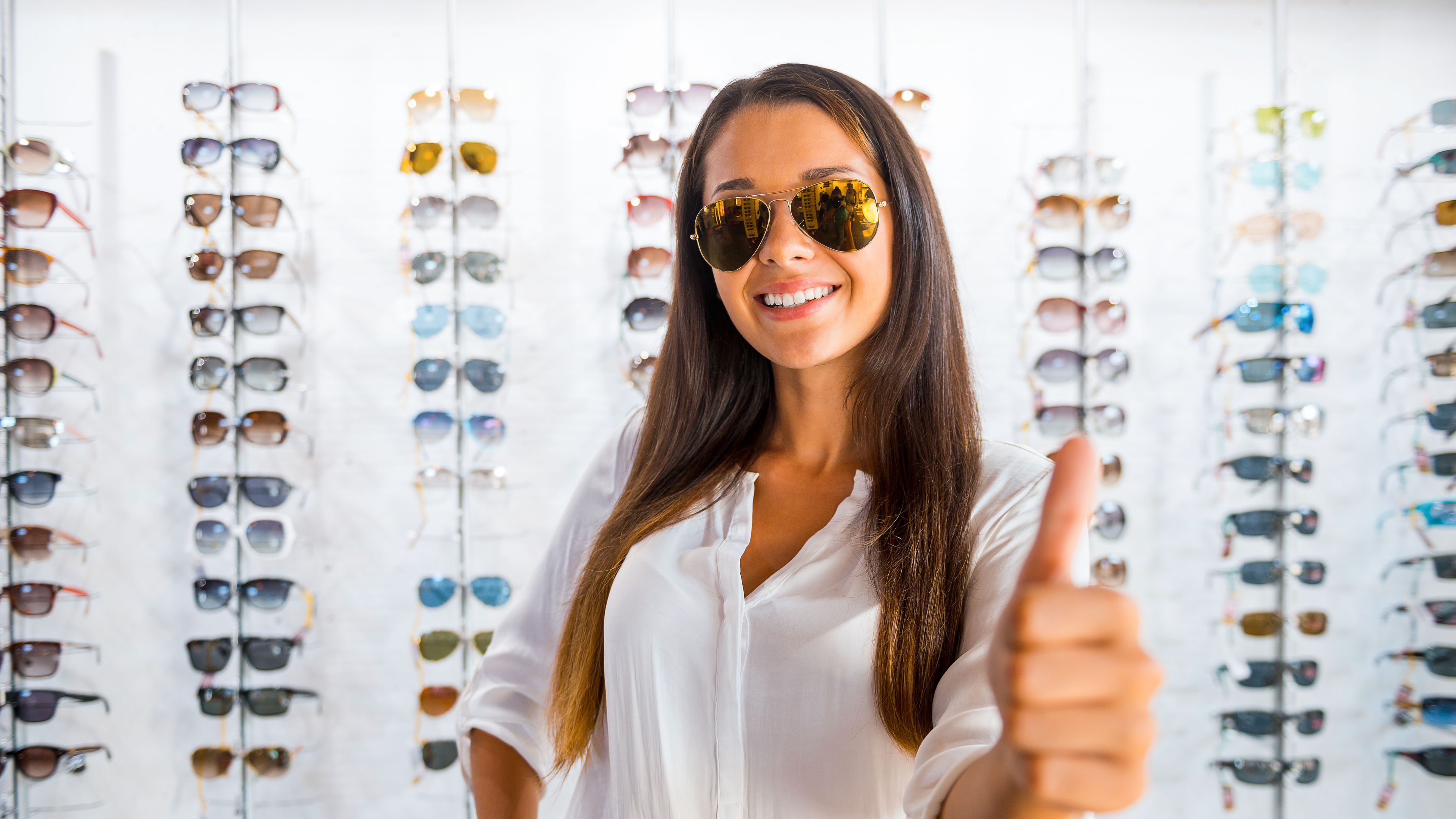 Confident woman in a stylish white outfit standing in front of a display of eyeglasses
