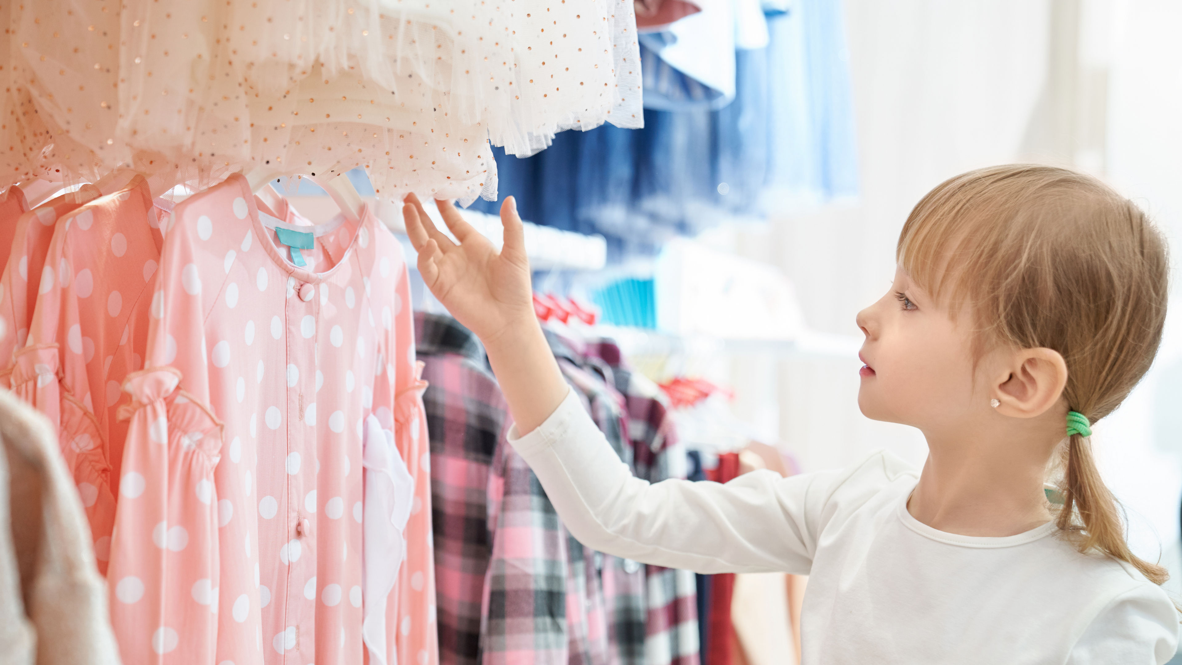 Girl in a white sweater looking at a pink dress