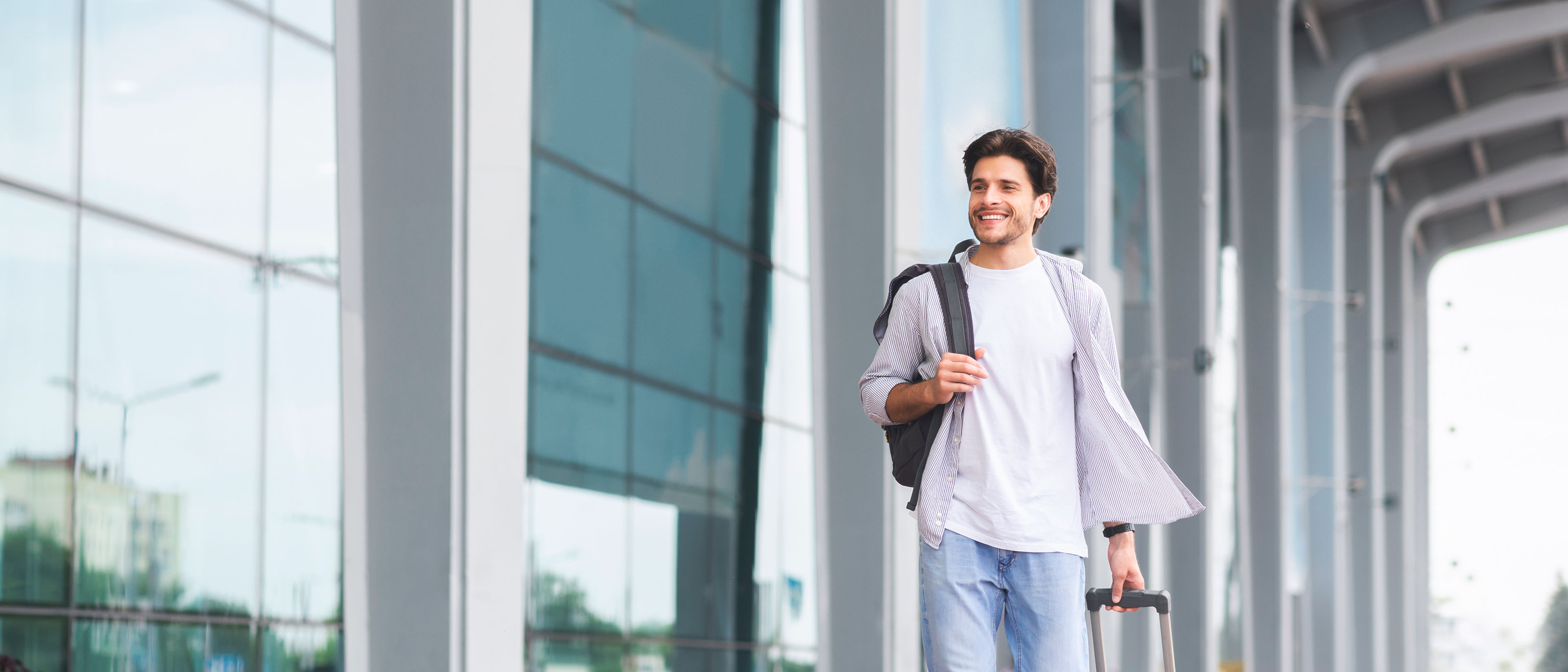 Happy man walking with luggage near modern airport building