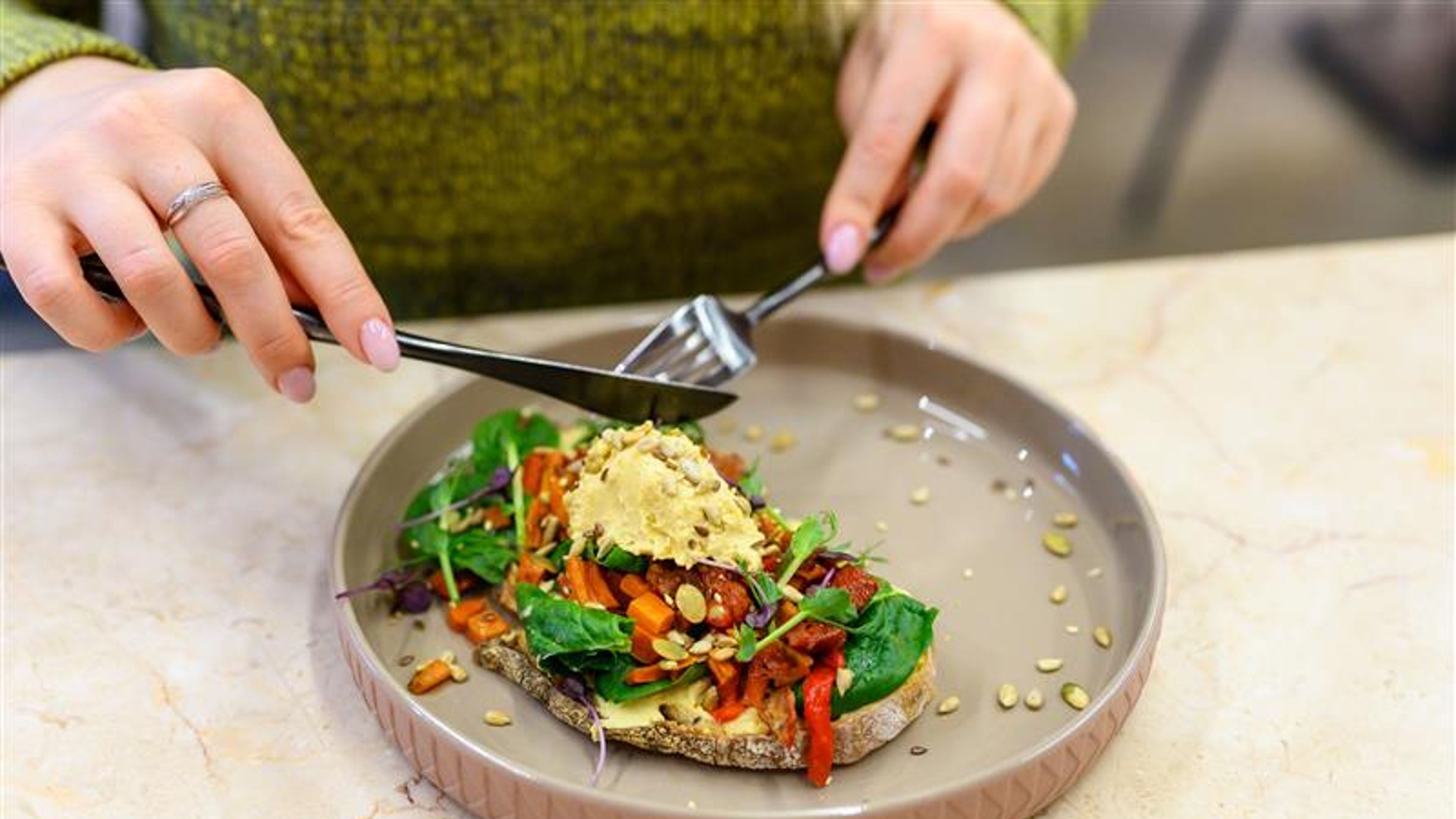 Homemade hummus on toast topped with baked vegetables, ready to be enjoyed by a woman