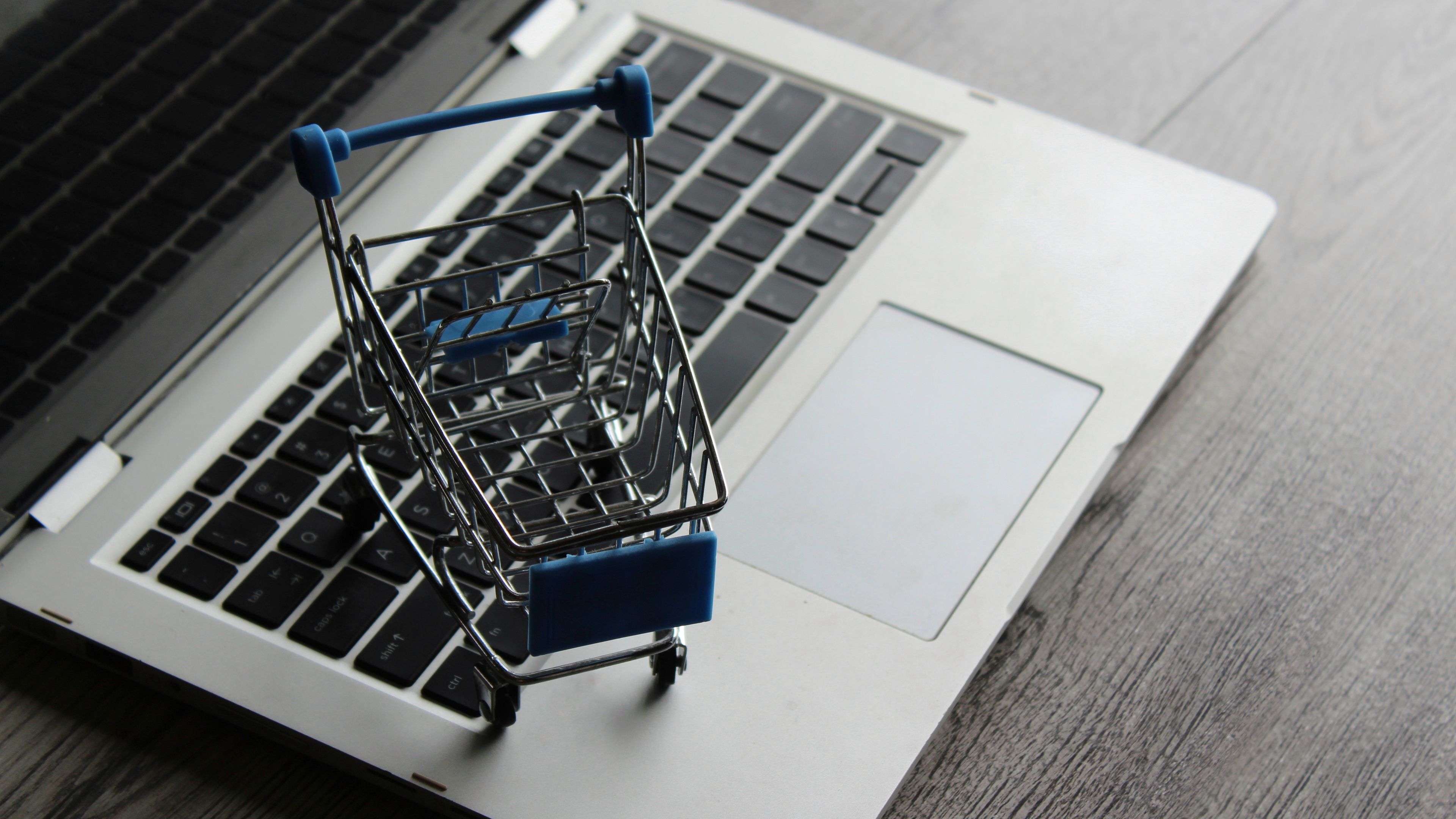 Laptop and mini shopping trolley on wooden table. 