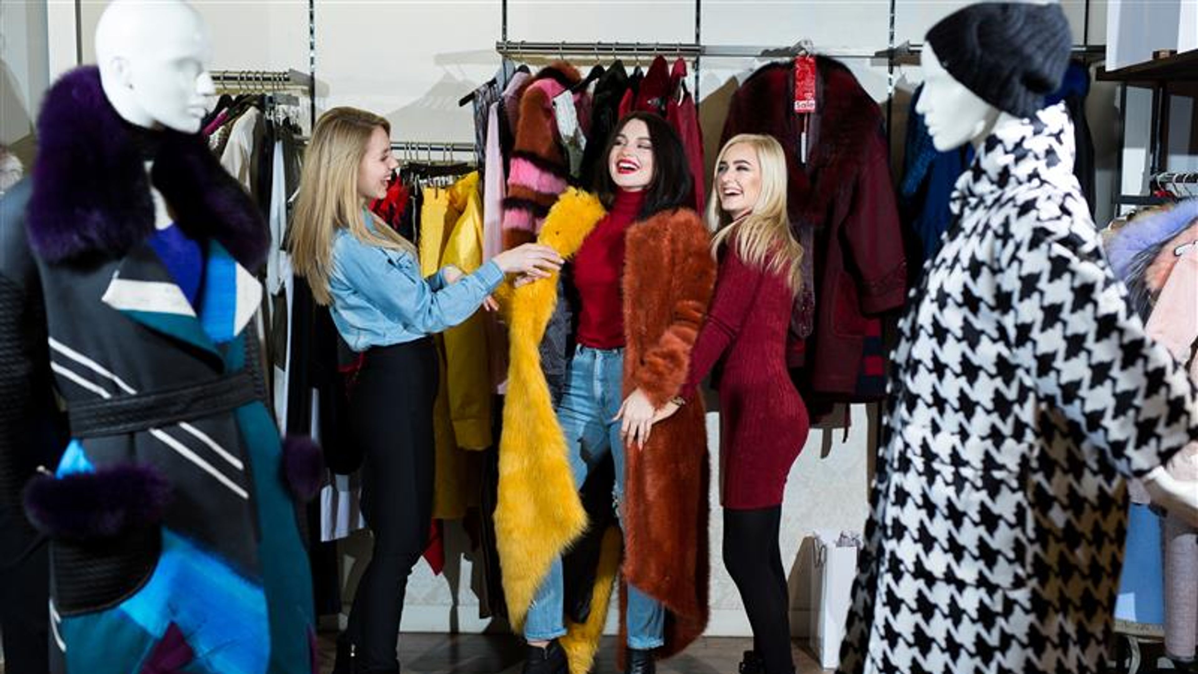 Three women are trying on a fur coat in the store