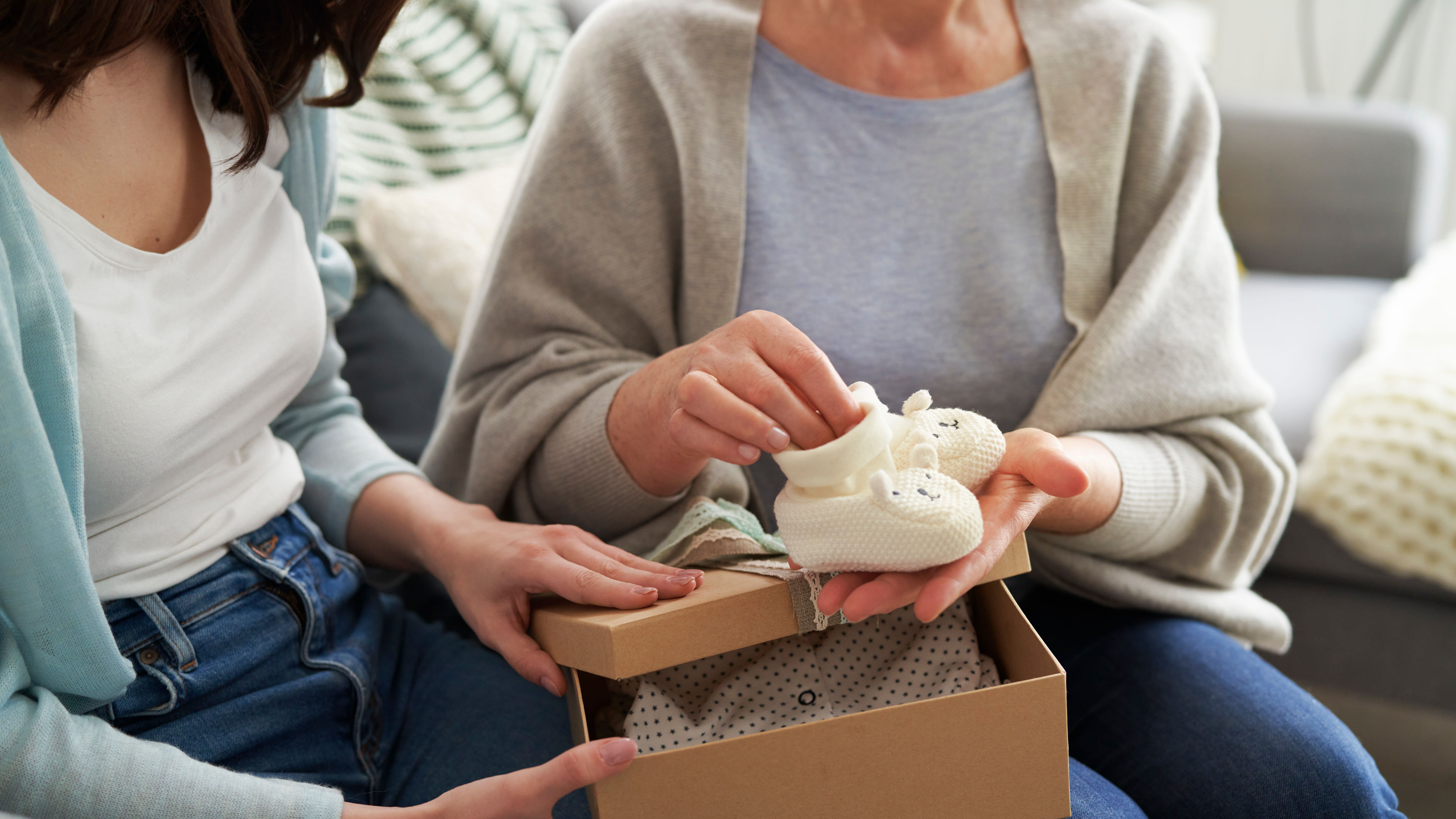 Two women sit together as one presents a gift box
