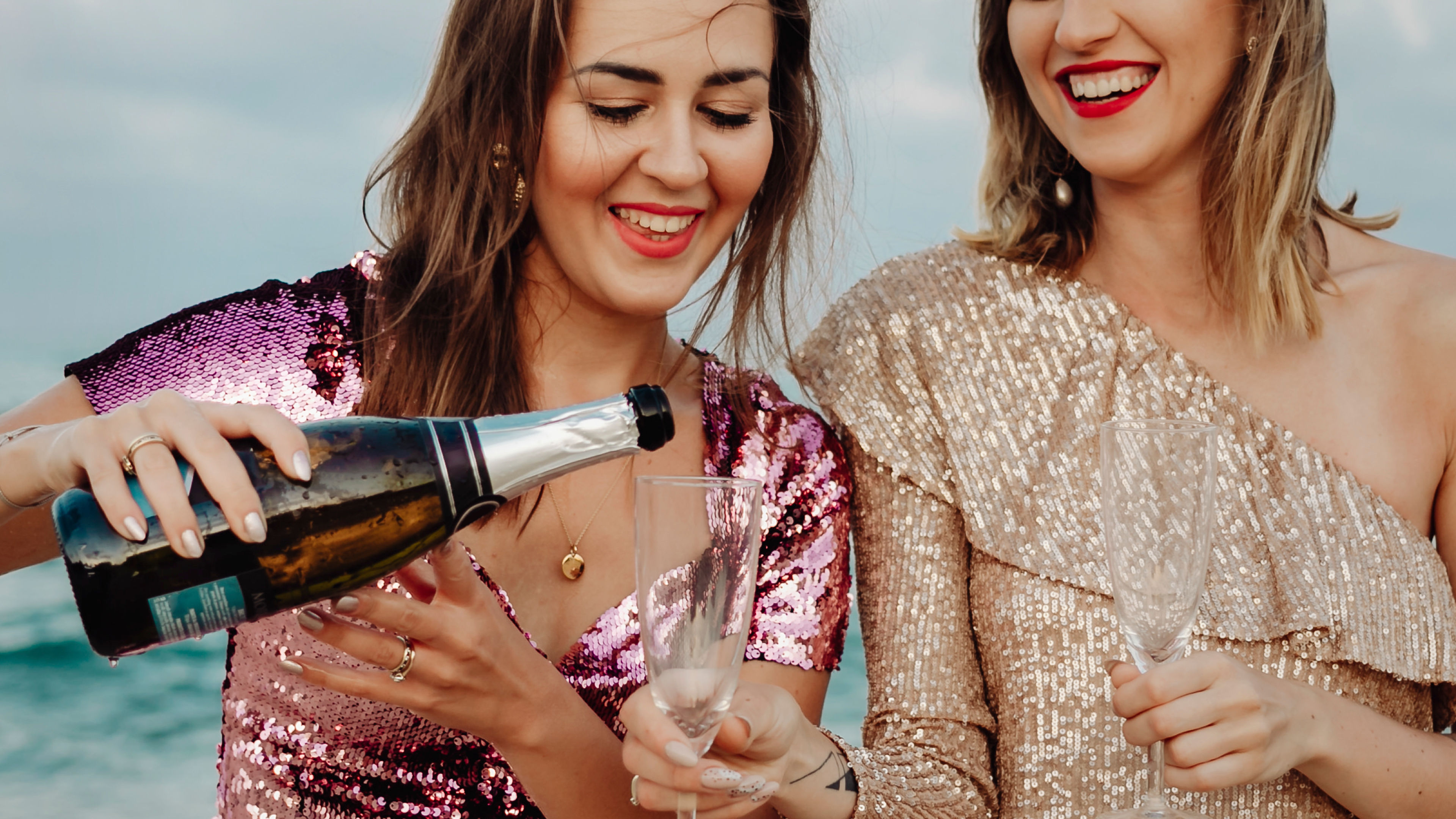 Women filling up a glass of champagne at the beach